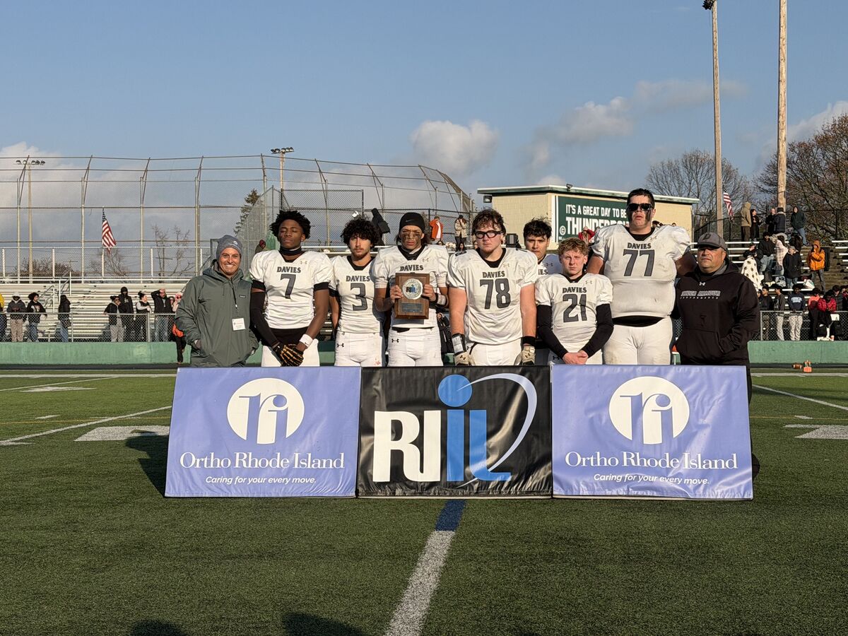 A football team poses with a trophy on a sunny day at a football field.