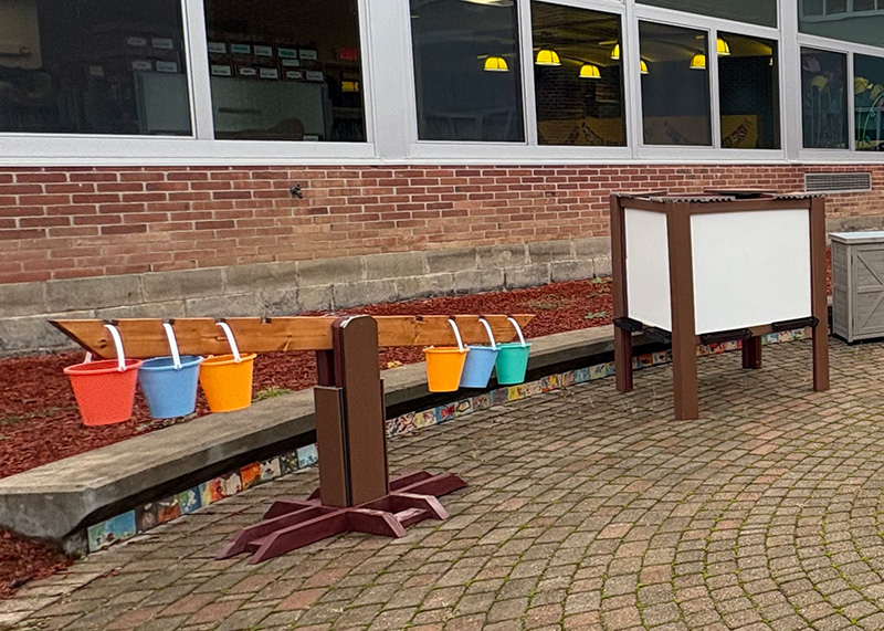 Outdoor play area with colorful buckets hanging from a wooden structure.