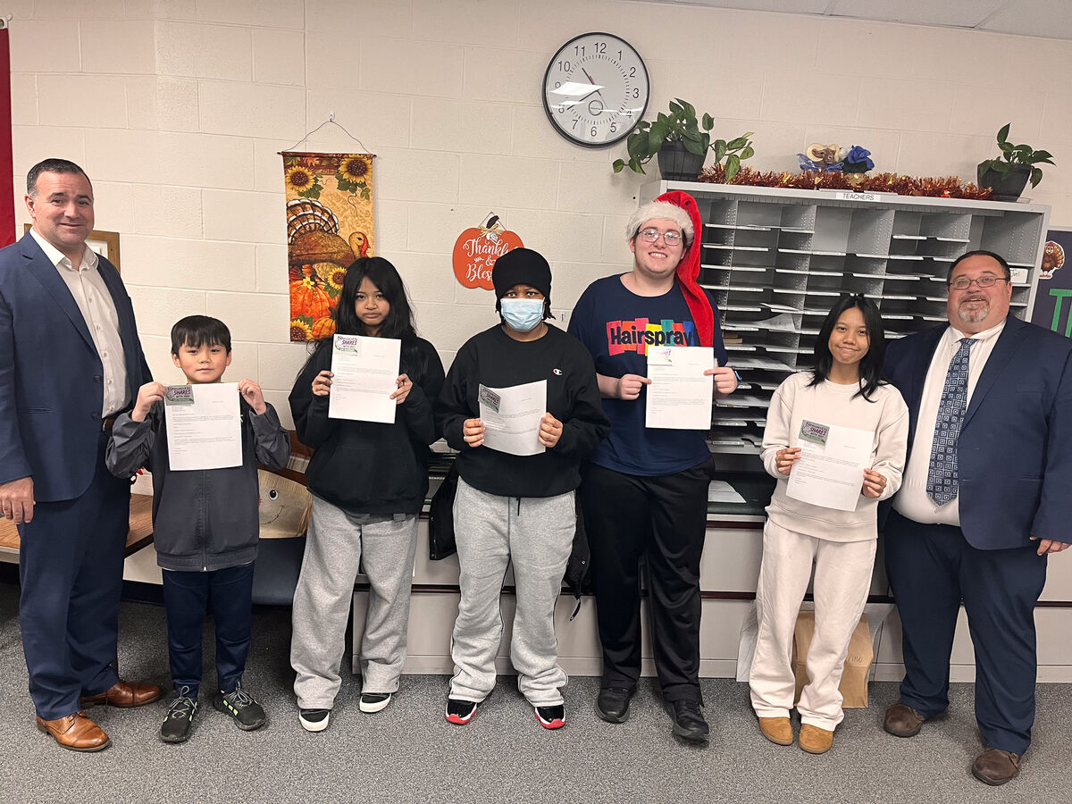A group of people, including students and adults, hold papers in a school setting.
