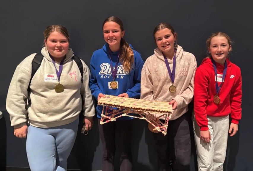 Four young people stand together, each wearing a medal and smiling.