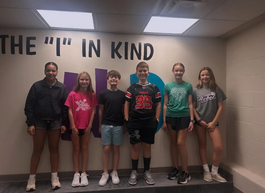 Six children stand together in front of a wall with text.