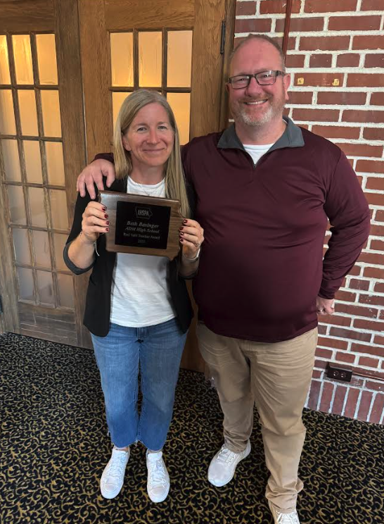 Two people pose for a photo, one holding an award plaque.