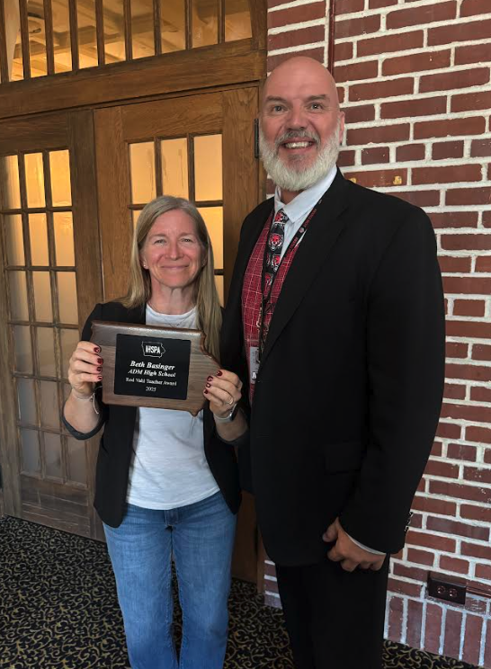 Two people pose for a photo, one holding an award plaque.