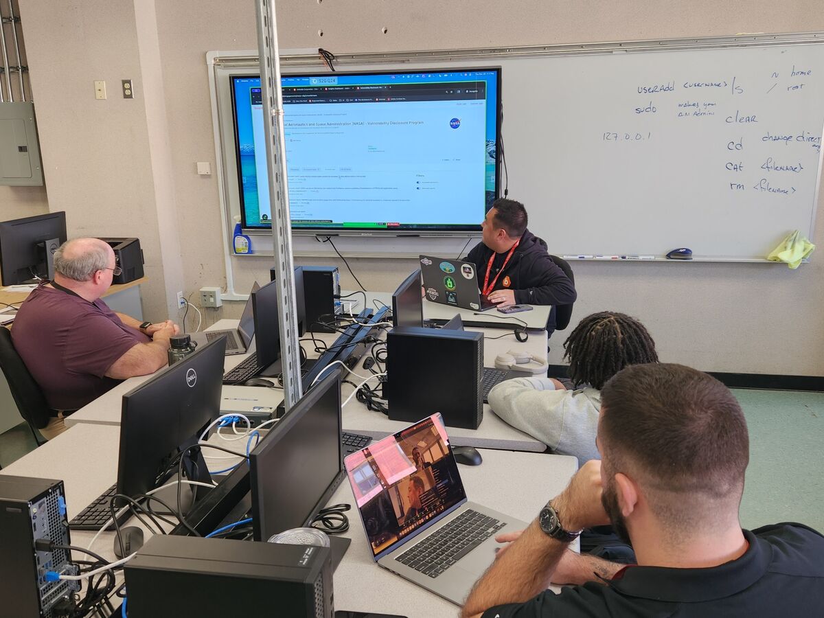A classroom setting with students working on computers, a presentation on a screen.