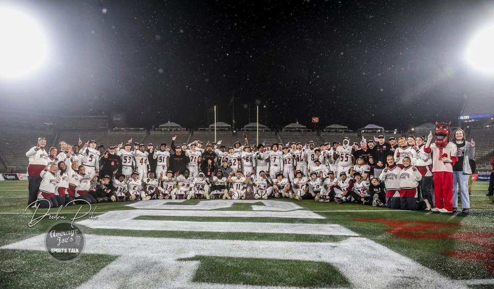 A large group of football players and cheerleaders pose on a football field at night.