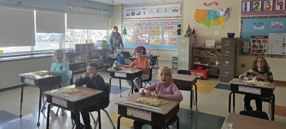 Children sit at desks in a classroom, each with a pile of popcorn.