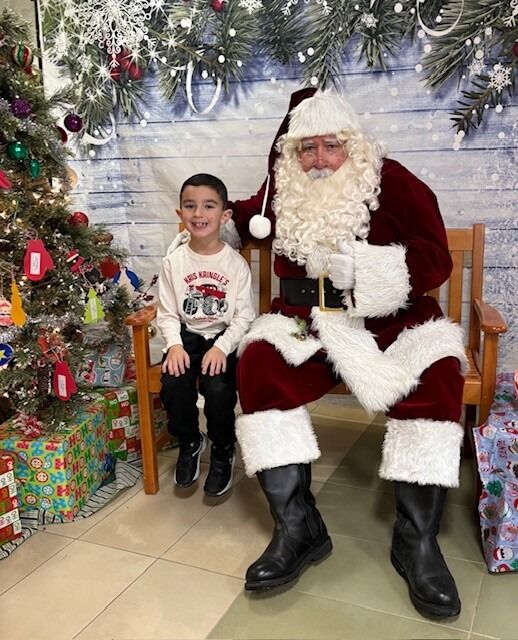 A young boy sits with Santa Claus, smiling for the camera.