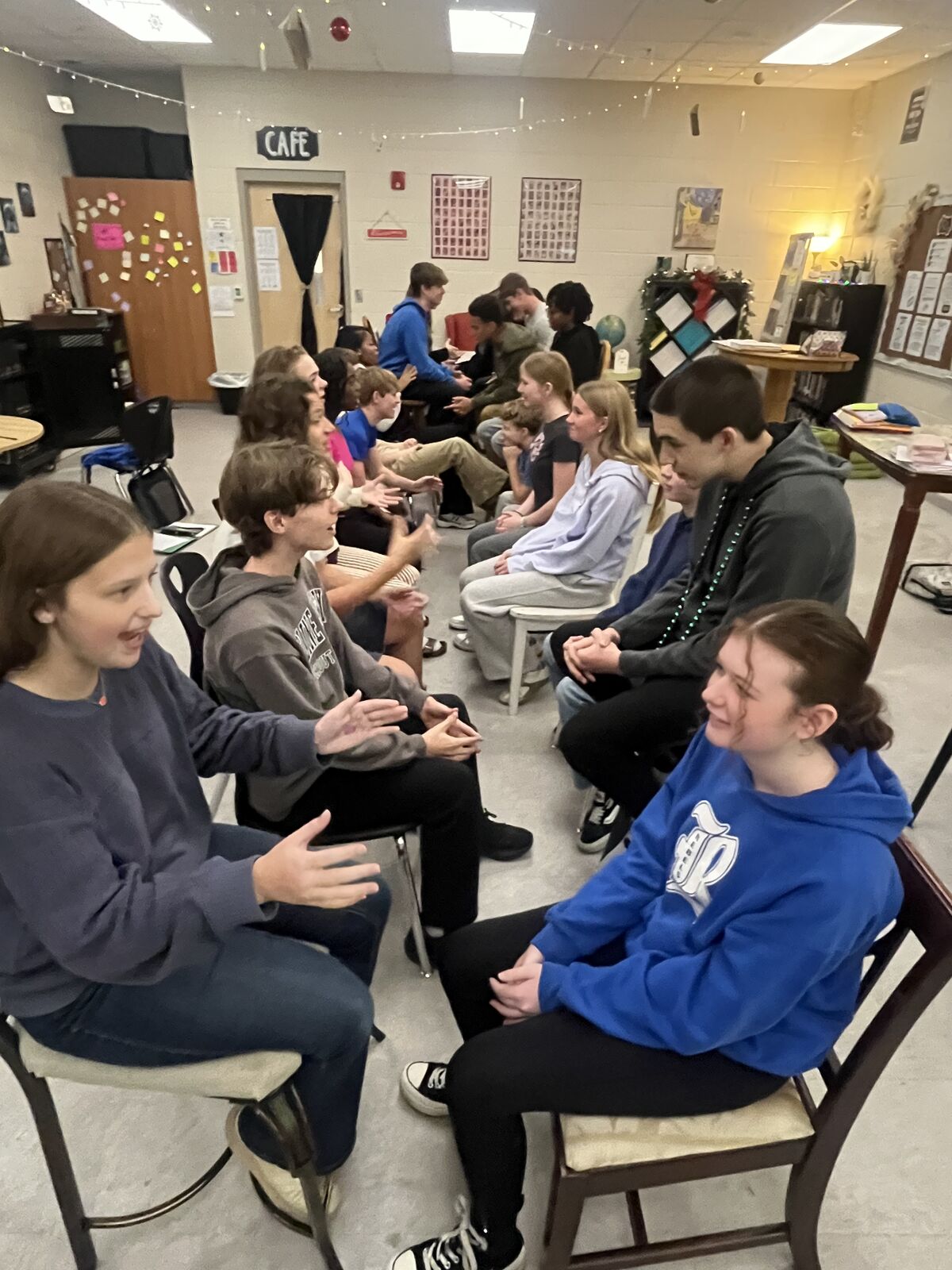 A group of students are seated in a room, possibly a classroom or cafe.