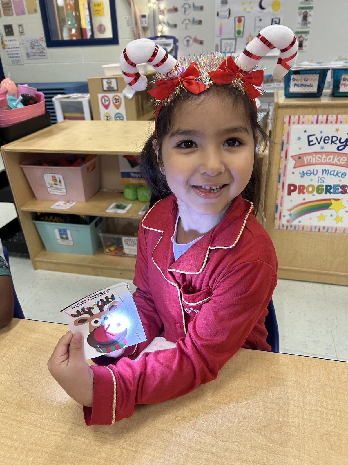 A young girl smiles, wearing a candy cane headband and holding a 'Magic Reindeer' card.