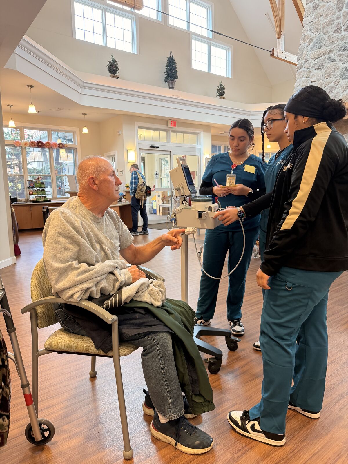 Healthcare professionals assist an elderly man in a bright, open space. Angelique Ibanez, Rhaissa Dias, Brissa Paredes Estrada