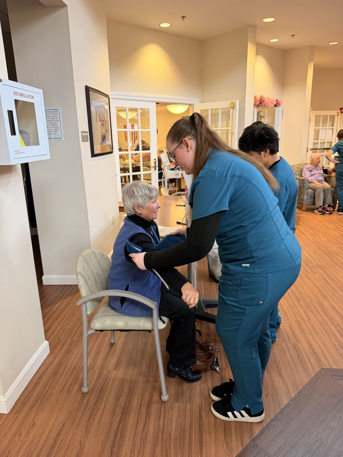 A healthcare worker assists an older adult in a well-lit room. Briana Voisinet, Daniel Diaz