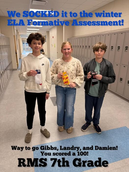Three students stand in a school hallway, holding socks and smiling.