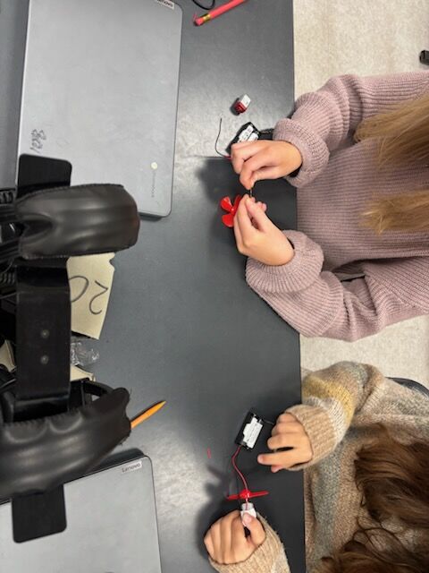 Two students work on a project at a table, assembling small components.