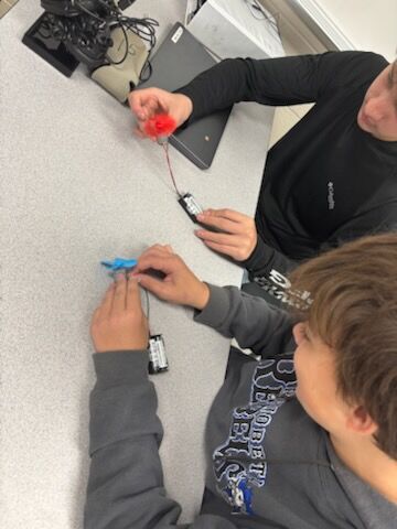 Two people work on a science project, connecting wires to batteries.