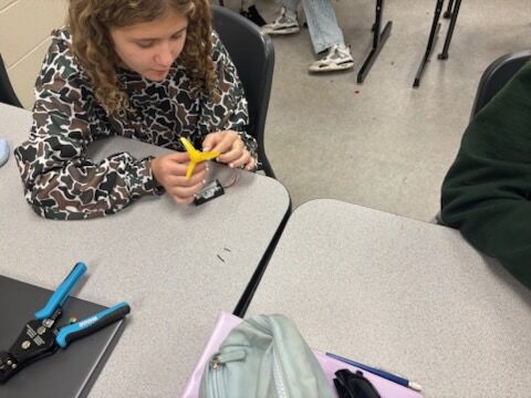 A student works on a project at a desk, assembling a small device.