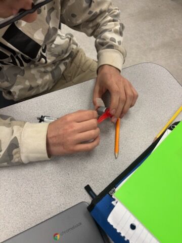 A student uses a compass and pencil on a desk.