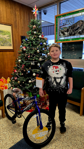 A young boy stands proudly next to a new blue bicycle and a decorated Christmas tree.
