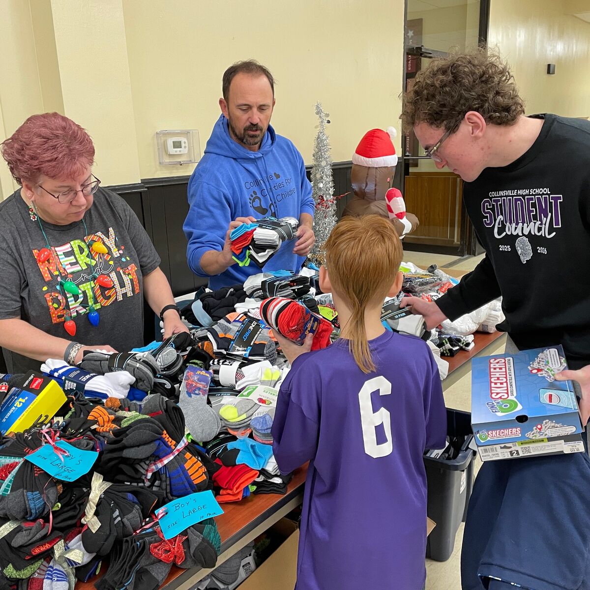 Volunteers sort through piles of socks and shoes for a donation drive, with holiday decorations in the background.