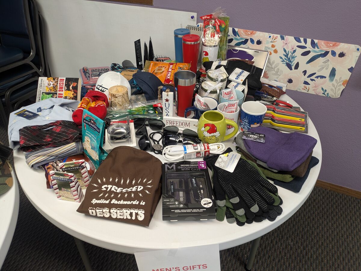 A round table displays a variety of men's gifts, including clothing, mugs, and grooming items.