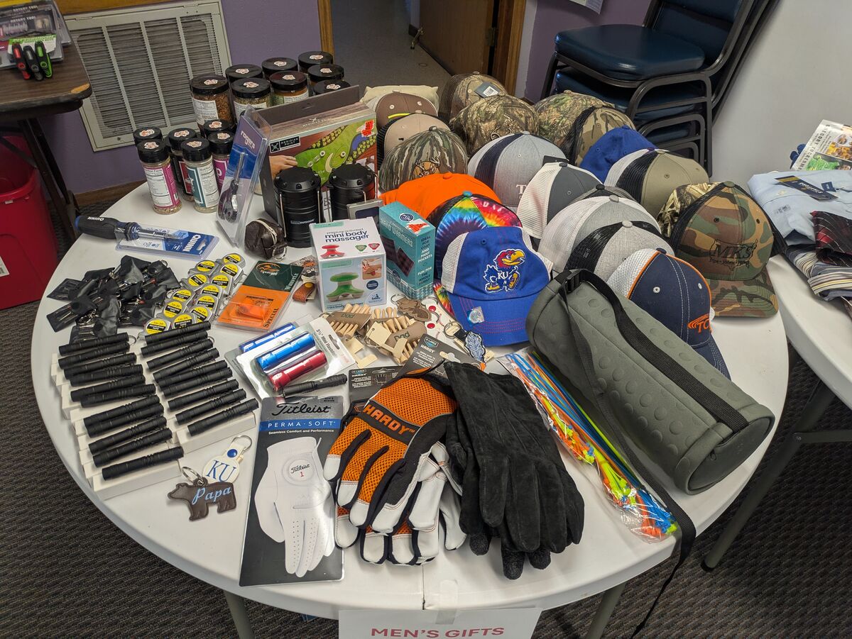 A round table displays a variety of men's gifts including hats, gloves, flashlights, and tools.