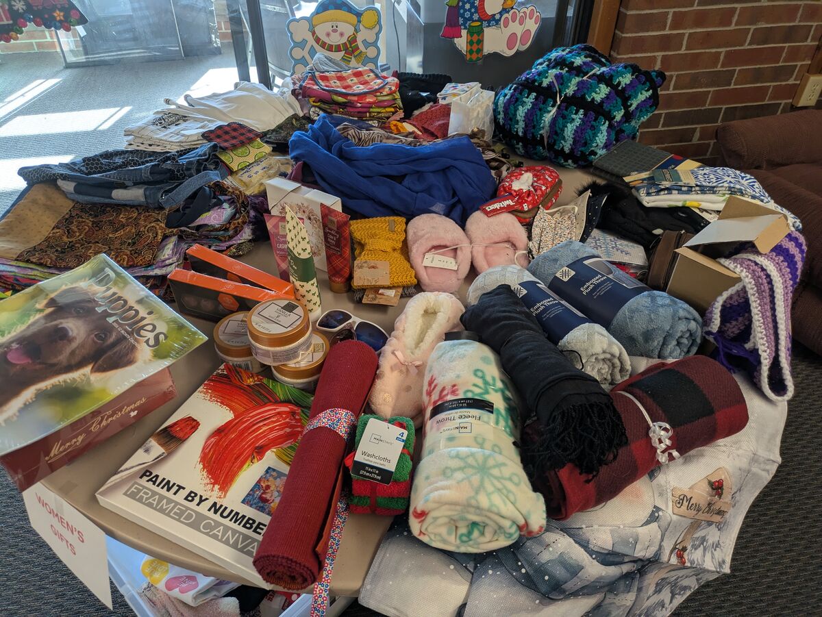 A table is covered with a variety of items including blankets, slippers, bath products, and a 'Puppies' calendar.