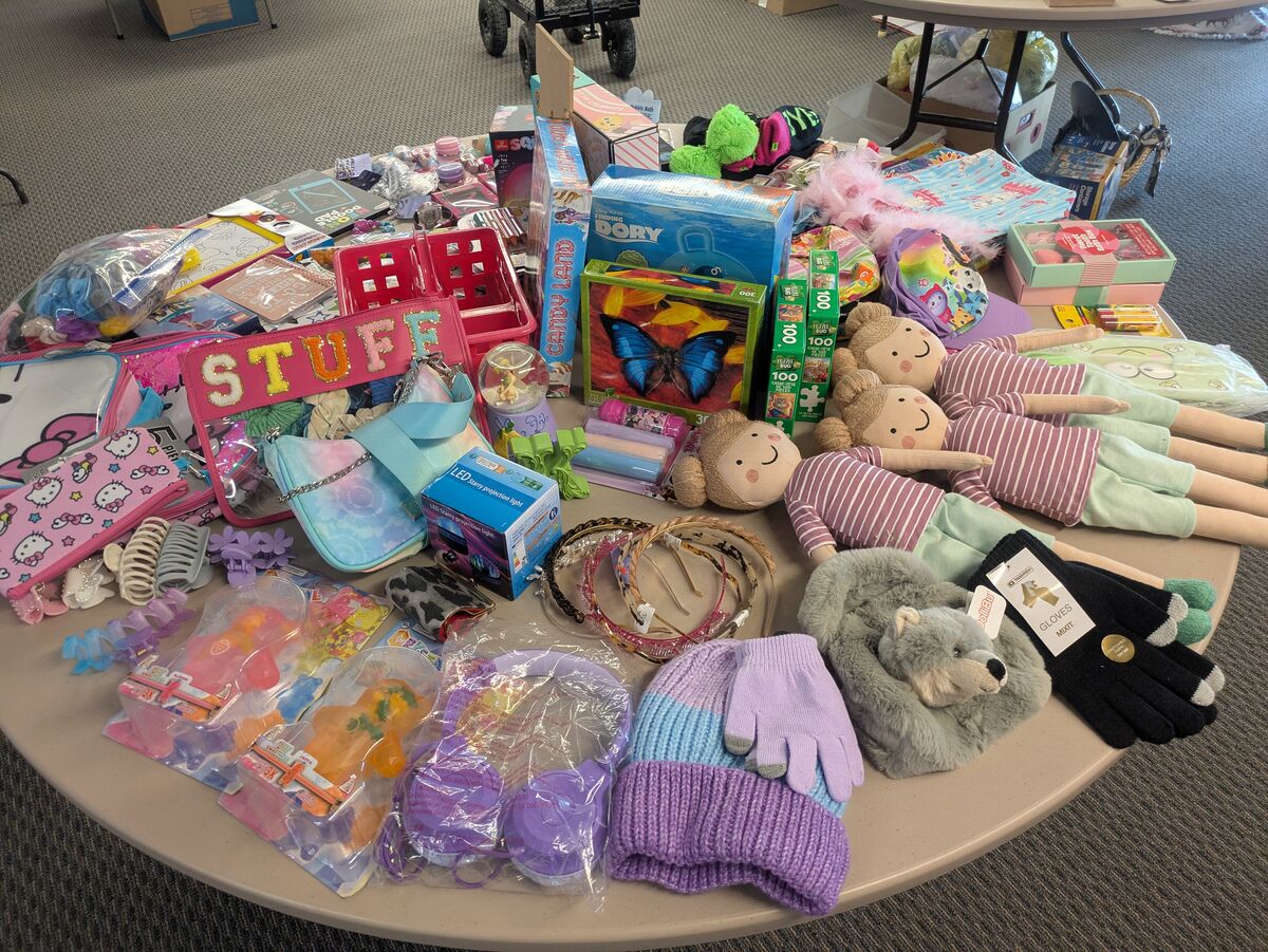 A collection of children's toys and accessories, including dolls, puzzles, hair clips, and hats, are spread across a round table.