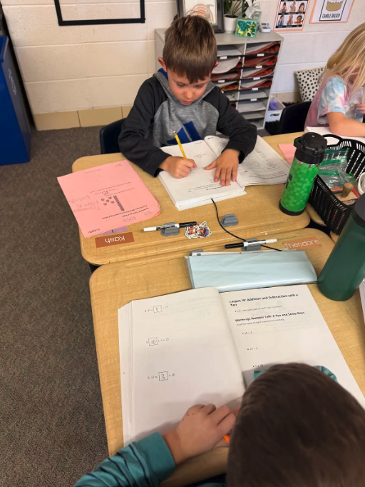 A young boy focuses intently on his math worksheet at a classroom desk.