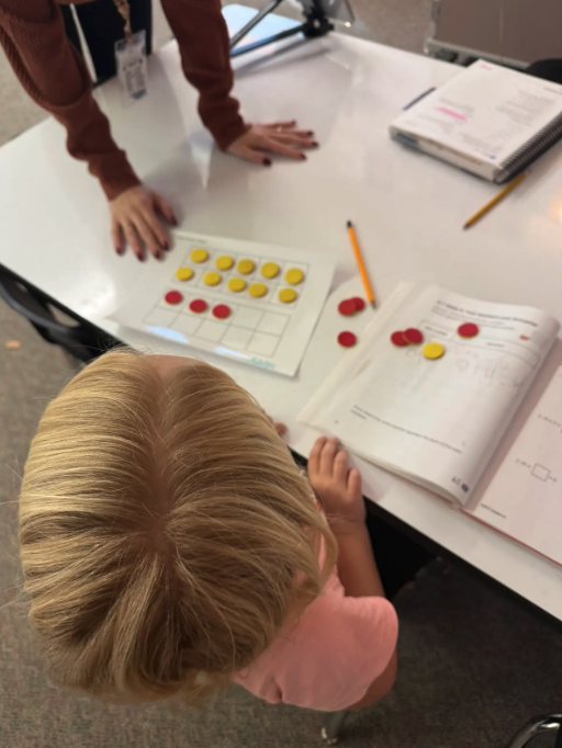 A child learns math with red and yellow counters on a ten-frame mat.