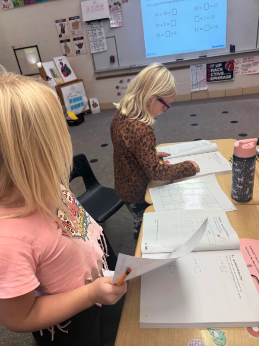 Two young students focus on math worksheets at their desks in a classroom.