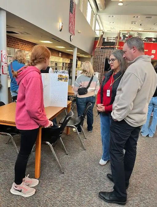 A young person presents a project to adults at a school event.