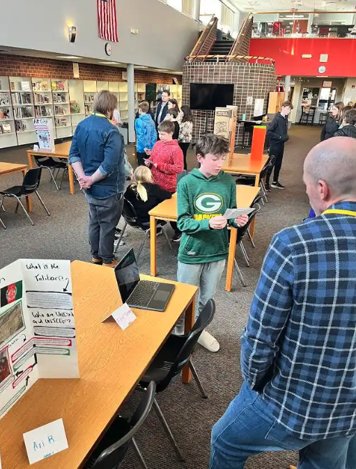 Students present projects at tables in a school library.