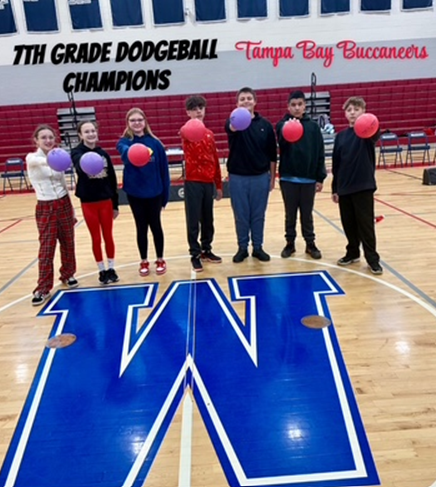 Six students, the 7th Grade Dodgeball Champions, pose with dodgeballs on a gym floor with a large 'W' logo.