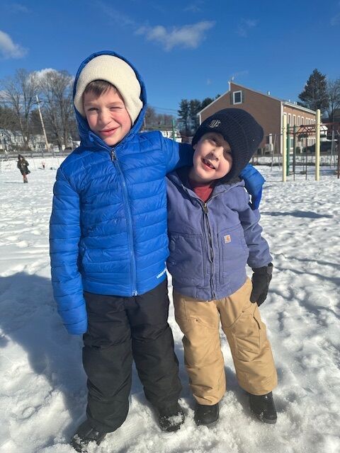 Two smiling boys in winter jackets and hats pose in the snow.