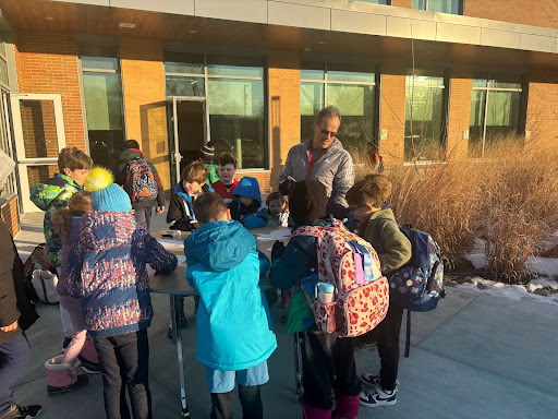 Mr. Guzzi stands at table welcoming students to school as part of the penguin promenade. 