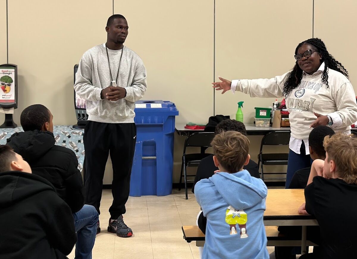 A man and a woman address a group of young people seated at tables.