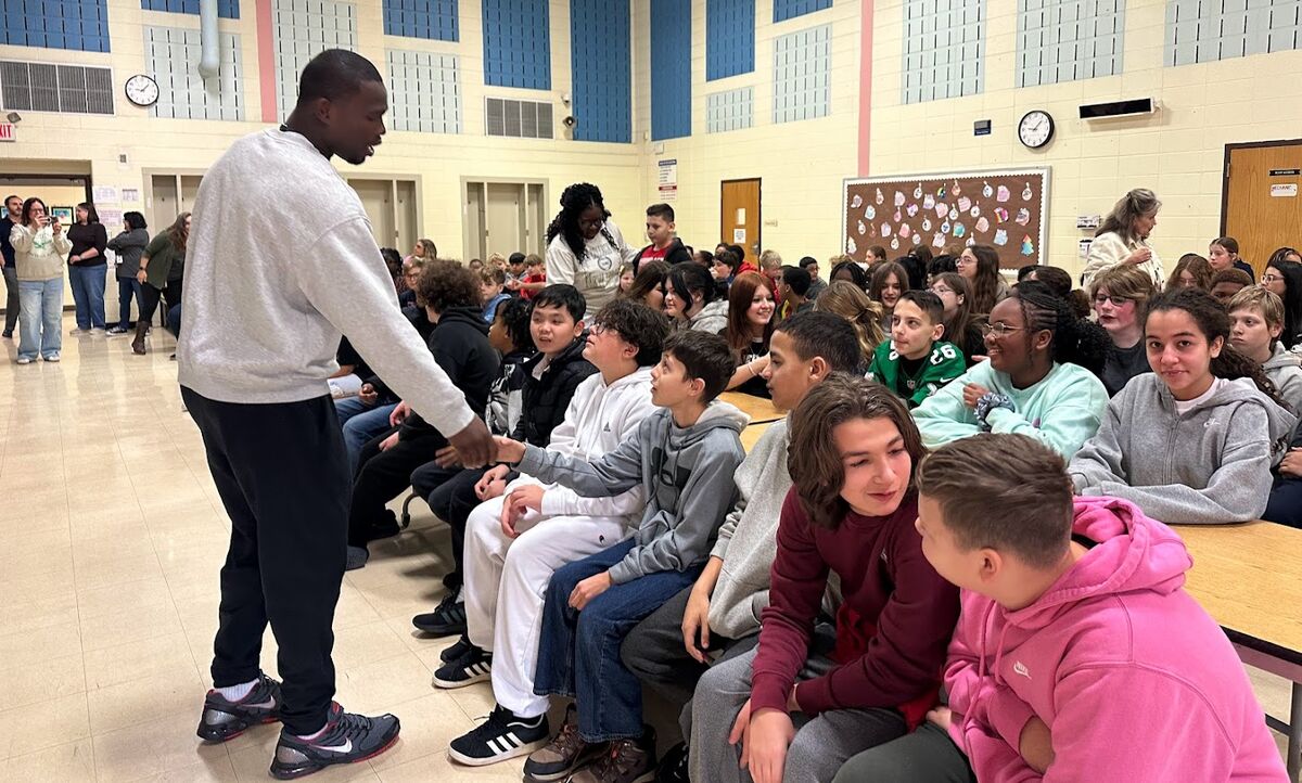 A man in a grey sweatshirt shakes hands with students seated in an auditorium.