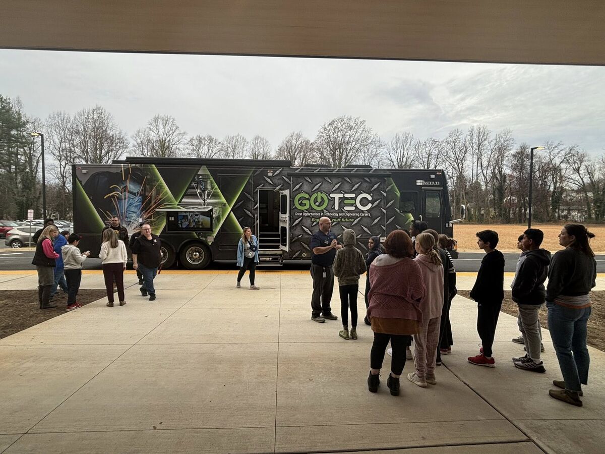 A group of students gathers around a bus labeled 'GoTEC' for a presentation on technology and engineering careers.