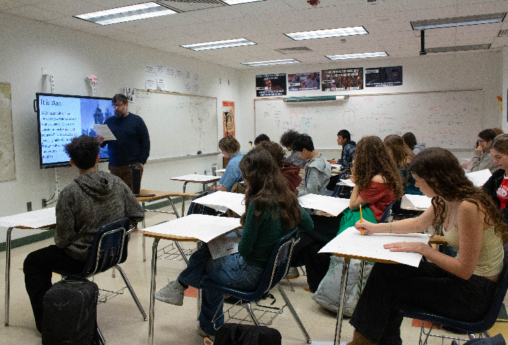 Mr. Andrew Everton stands by a large screen presenting information to a classroom of students.