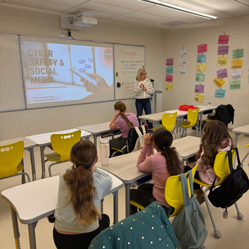 A teacher presents a lesson on "Cyber Safety & Social Media" to students in a classroom.