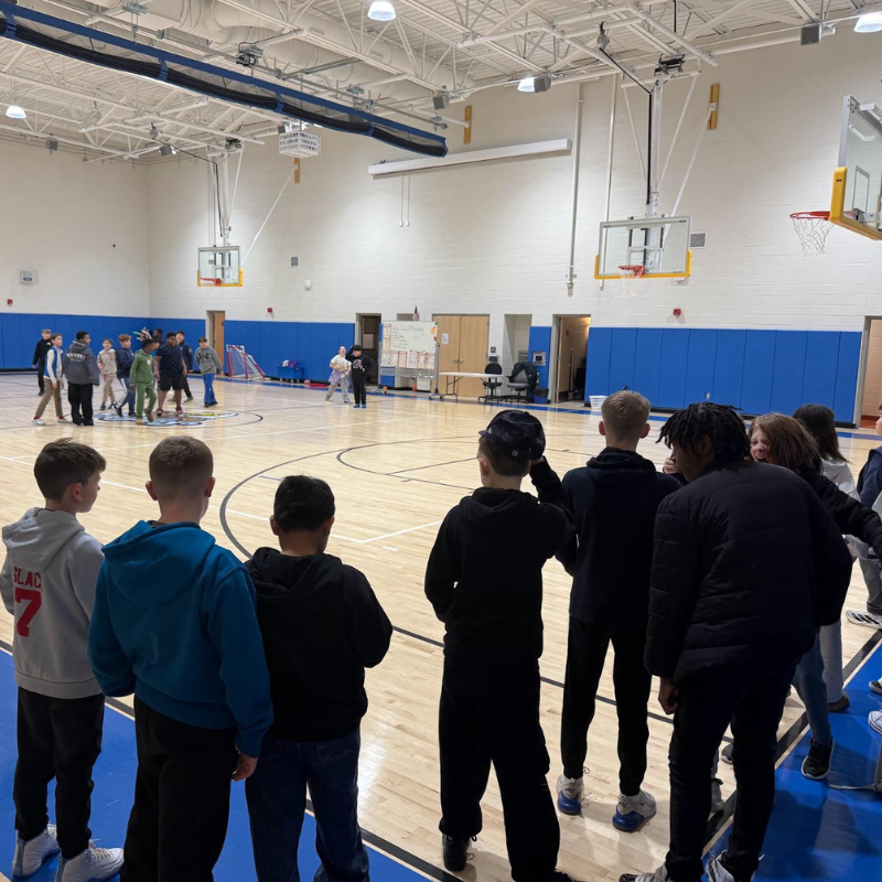 A group of children stand on a basketball court, facing away from the camera.