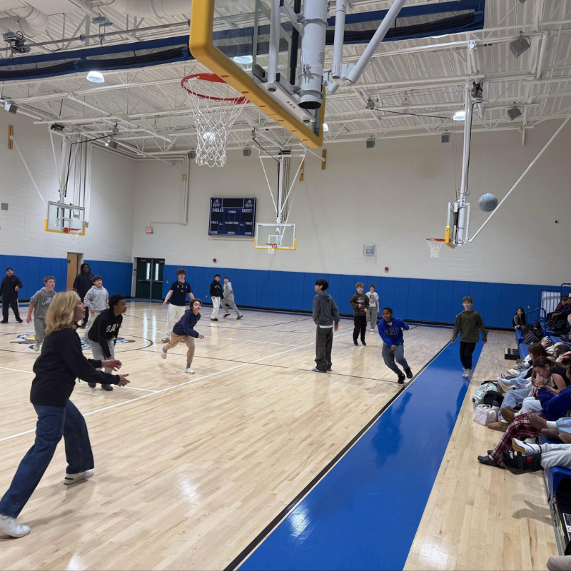 Students engage in a basketball game on a polished wooden court in a gymnasium.