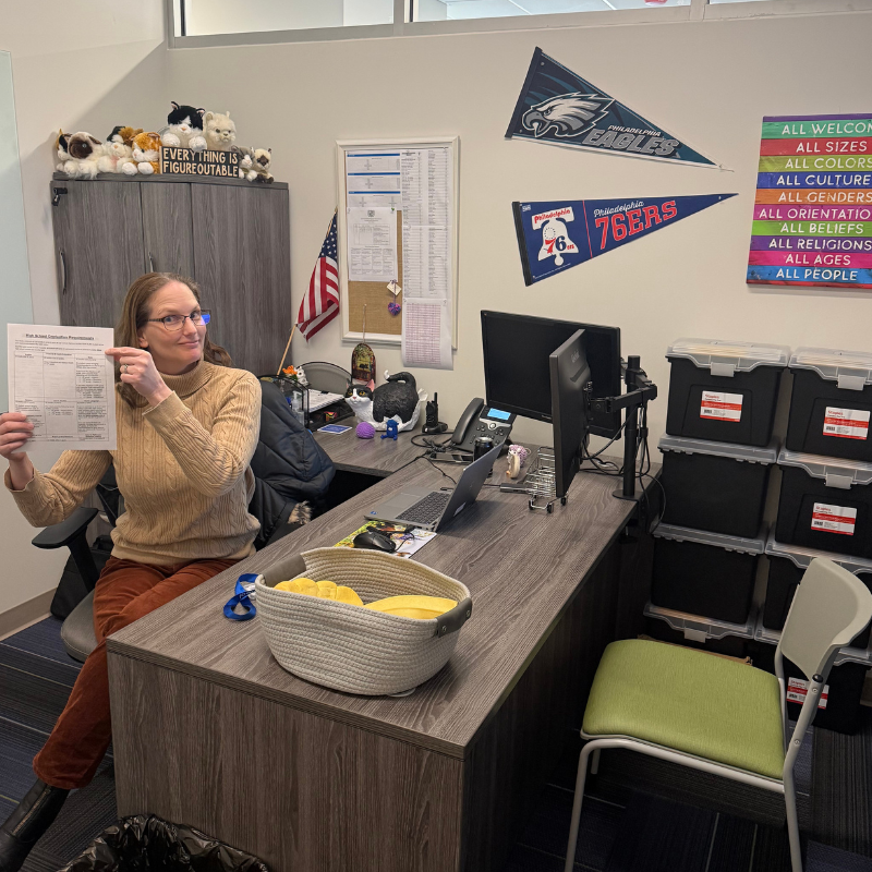 A woman in glasses points to a document titled 'High School Graduation Requirements' in an office.