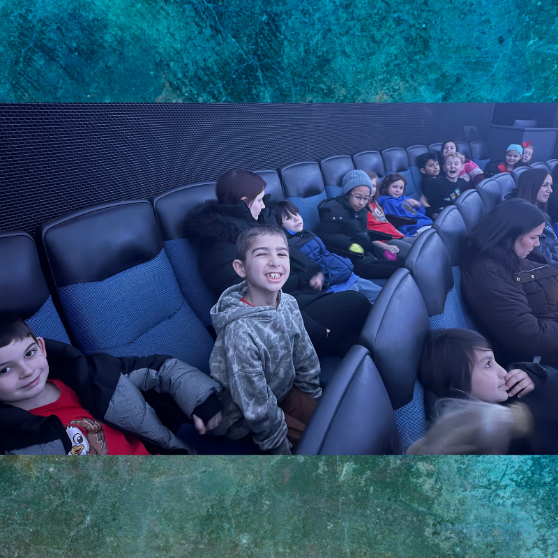 A group of children and adults are seated in a theater, looking towards the front.