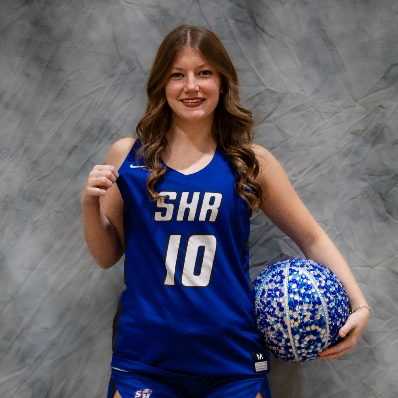 A young woman in a blue basketball jersey with the number 10 holds a decorated basketball.