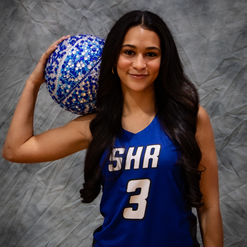 A young woman in a blue basketball jersey with the number 3 holds a decorative basketball.