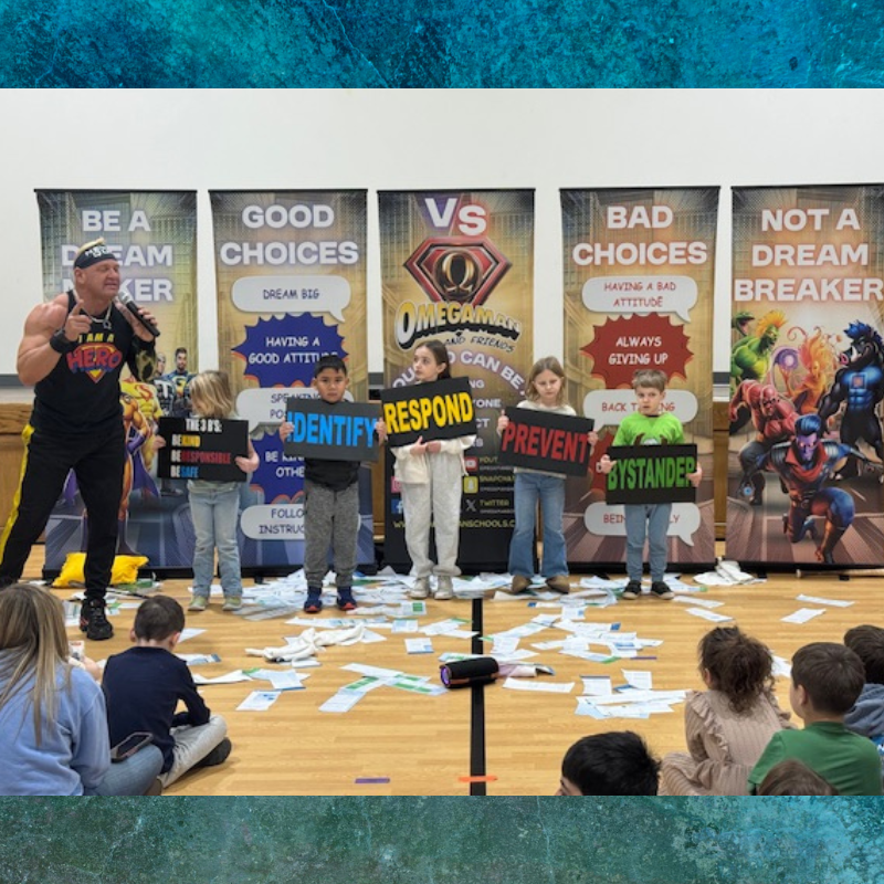 A muscular man in a superhero costume speaks to children holding signs that say 'IDENTIFY', 'RESPOND', and 'PREVENT'.