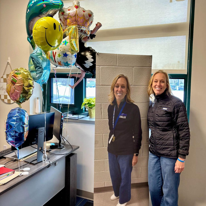 A cluster of colorful balloons, including a dolphin, smiley face, and crown, floats above an office desk.