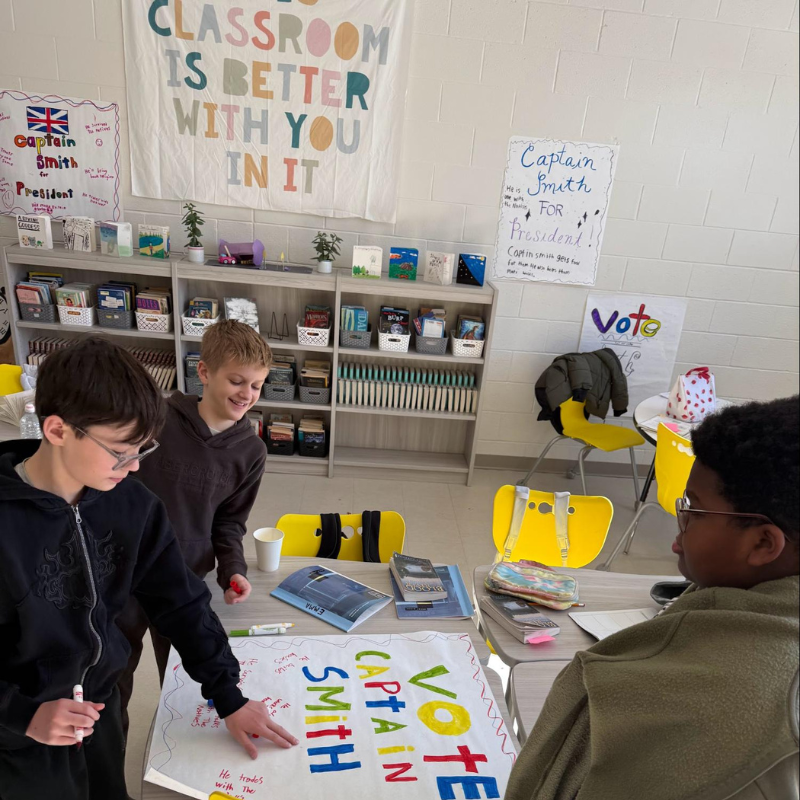 Students collaborate on a "Vote Captain Smith for President" poster in a classroom decorated with motivational banners.