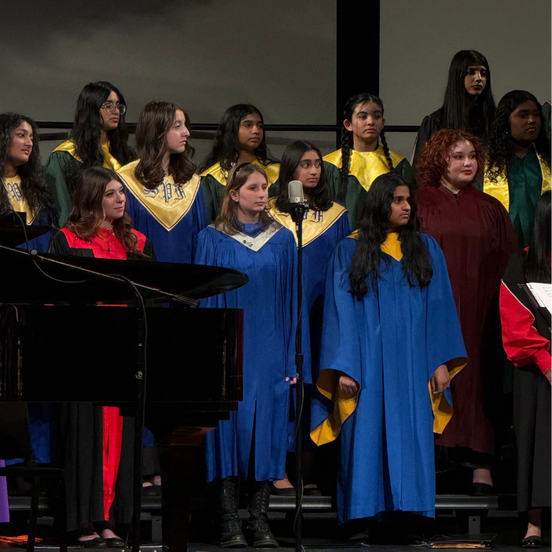 A diverse group of young people in blue and gold choir robes stand on risers, facing forward.