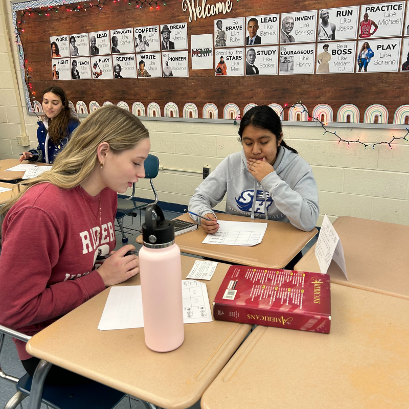 Students work at desks in a classroom, with inspirational posters of historical figures on the wall.